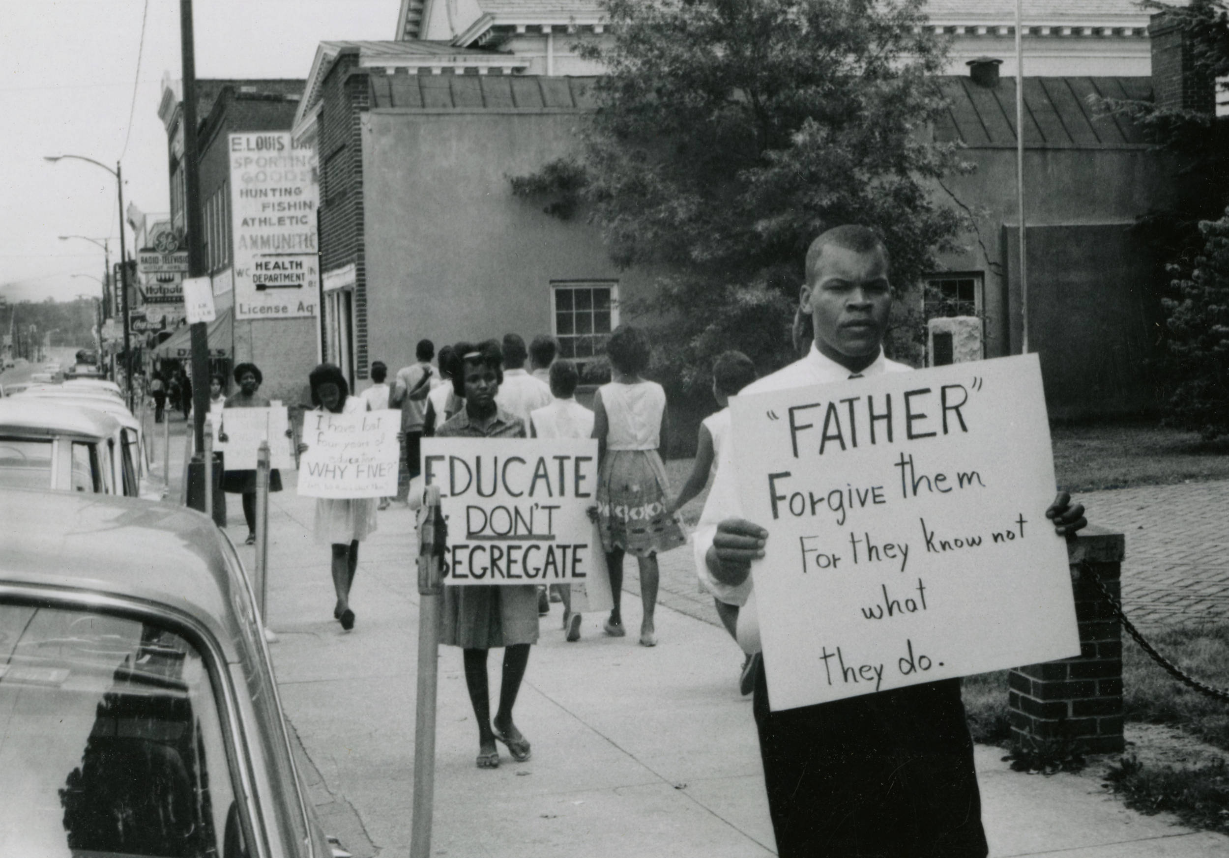 An image of peaceful demonstrators with picket signs denouncing segregation lining the sidewalks
